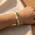 A beaded bracelet made of alternating off-white cylindrical beads and mint green spacer rings, displayed on a wooden measuring block marked 6in.