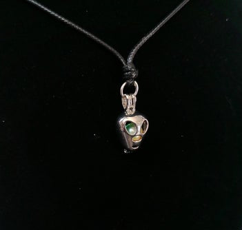 A silver pendant necklace featuring a skull with a green and yellow stone, displayed on a black velvet jewelry bust.