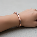 A beaded stretch bracelet made of small cylindrical wood beads in a warm copper or rose-gold tone, arranged in a circle on a dark textured background.