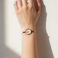 A pink cord bracelet with a round glass cabochon pendant featuring a pink flamingo design, displayed on a wooden measuring board with inch markings.
