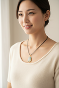 A teardrop-shaped pendant necklace displayed on a black velvet jewelry bust. The pendant features a gold-toned border and a light blue iridescent center with a white and gold illustration.