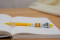 A yellow mechanical pencil with decorative beads, including a sugar skull bead, placed on a wooden measuring board with circular markings.