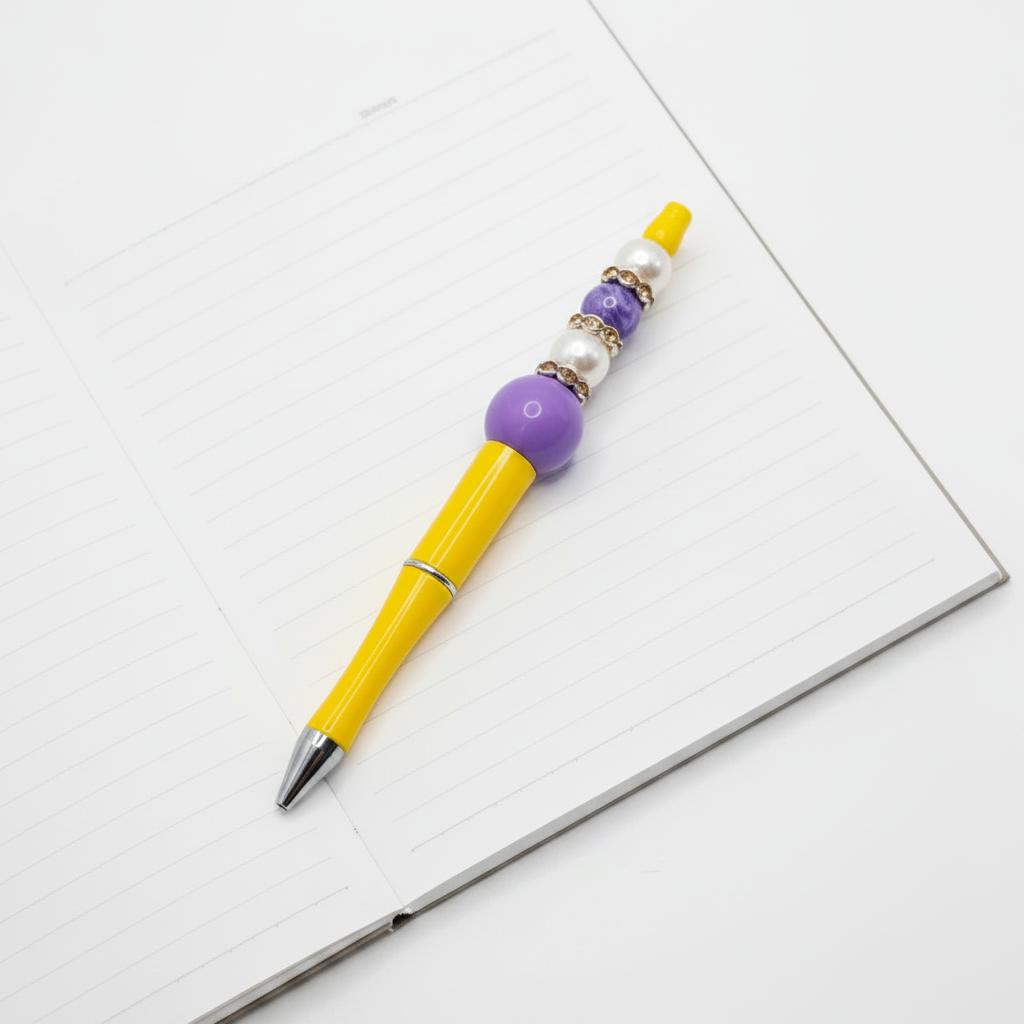 A yellow pen with purple and white beads, displayed on a wooden ruler with size markings.