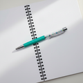 A turquoise and silver ballpoint pen with colorful rhinestones in the cap, resting on a wooden ruler with engraved size markings.
