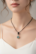 A silver-toned pendant necklace with a blue-green stone and black cord, displayed on a black velvet jewelry bust.