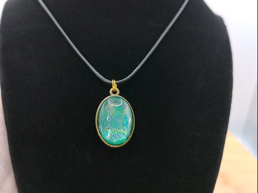 An oval pendant necklace with a green iridescent stone set in a gold-tone frame, displayed on a black velvet jewelry bust.