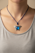 A silver butterfly pendant necklace with a blue marbled stone in the center, suspended on a blue cord, displayed on a black jewelry bust.