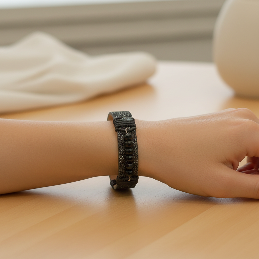 A handmade black beaded and glittery leather cuff bracelet displayed on a wooden measuring block marked with 6.5 inches.