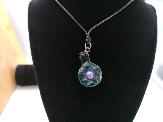 A circular glass pendant necklace with a purple gemstone at its center, hanging from a black cord on a black velvet display bust.
