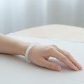 A translucent white beaded bracelet displayed on a wooden ring stand marked 6 inches, showing its circular shape and scale.