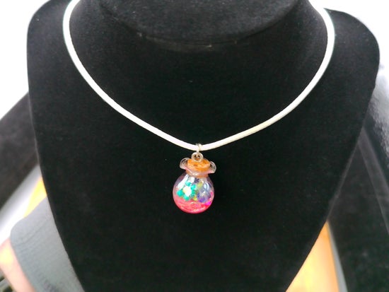 A white cord necklace with a small hanging charm shaped like a colorful potion bottle, displayed on a black velvet jewelry bust.