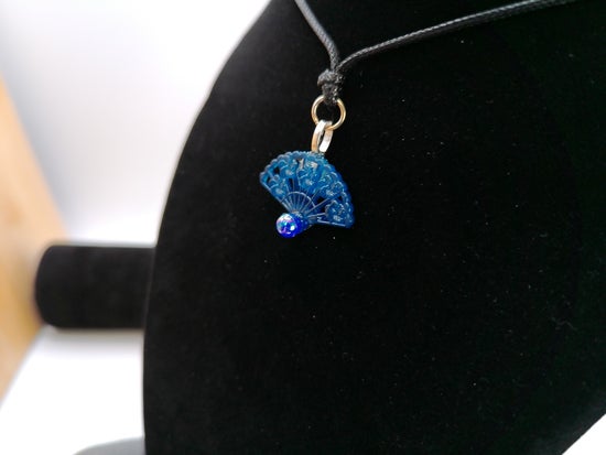 A small blue glass bead pendant on a silver chain, displayed on a black jewelry bust.
