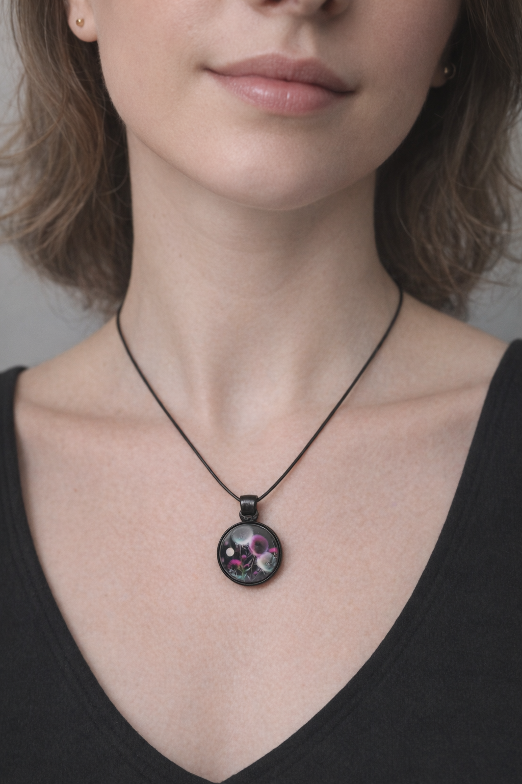 A close-up of a woman wearing a black cord necklace with a round pendant featuring a colorful floral design.