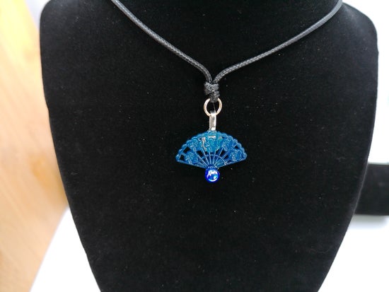 A blue butterfly pendant necklace displayed on a black neck stand against a white background.