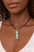 A close-up of a woman wearing a black cord necklace with a pointed pale green stone pendant in a silver-toned setting.